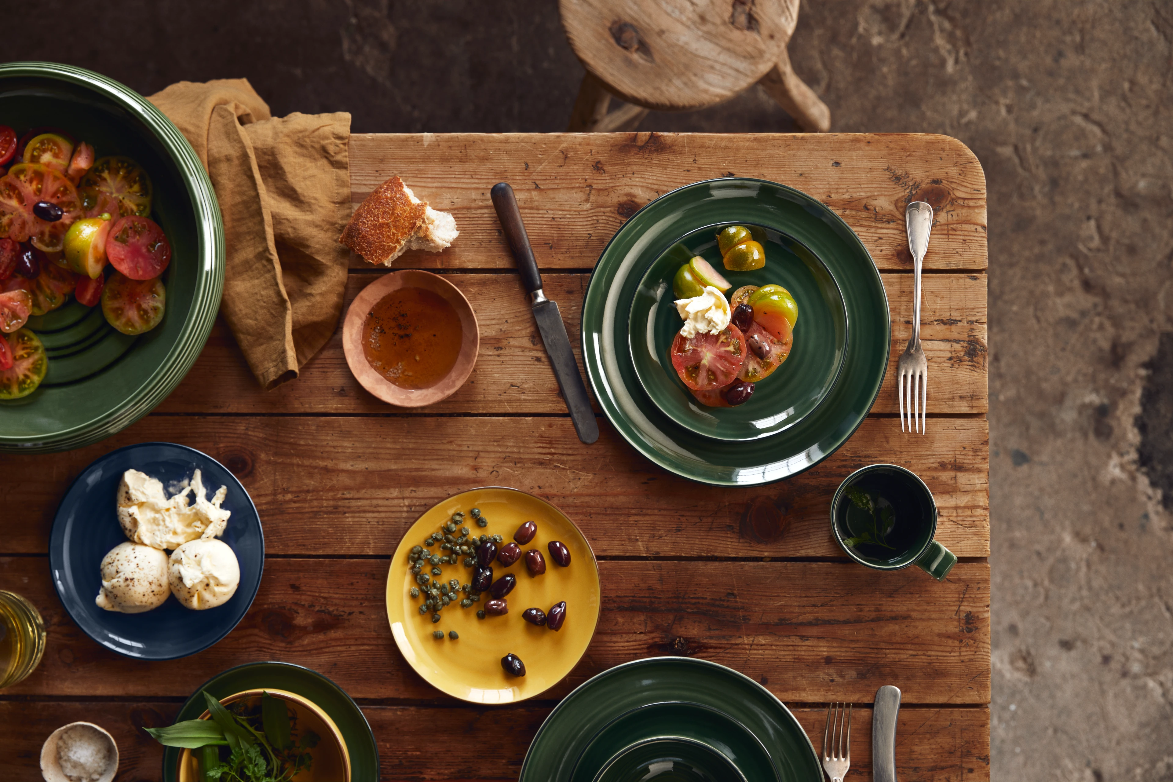 Tischgedeck mit bunten Tellern und kleinen Speisen aus Kähler Colore auf rustikalem Holztisch
