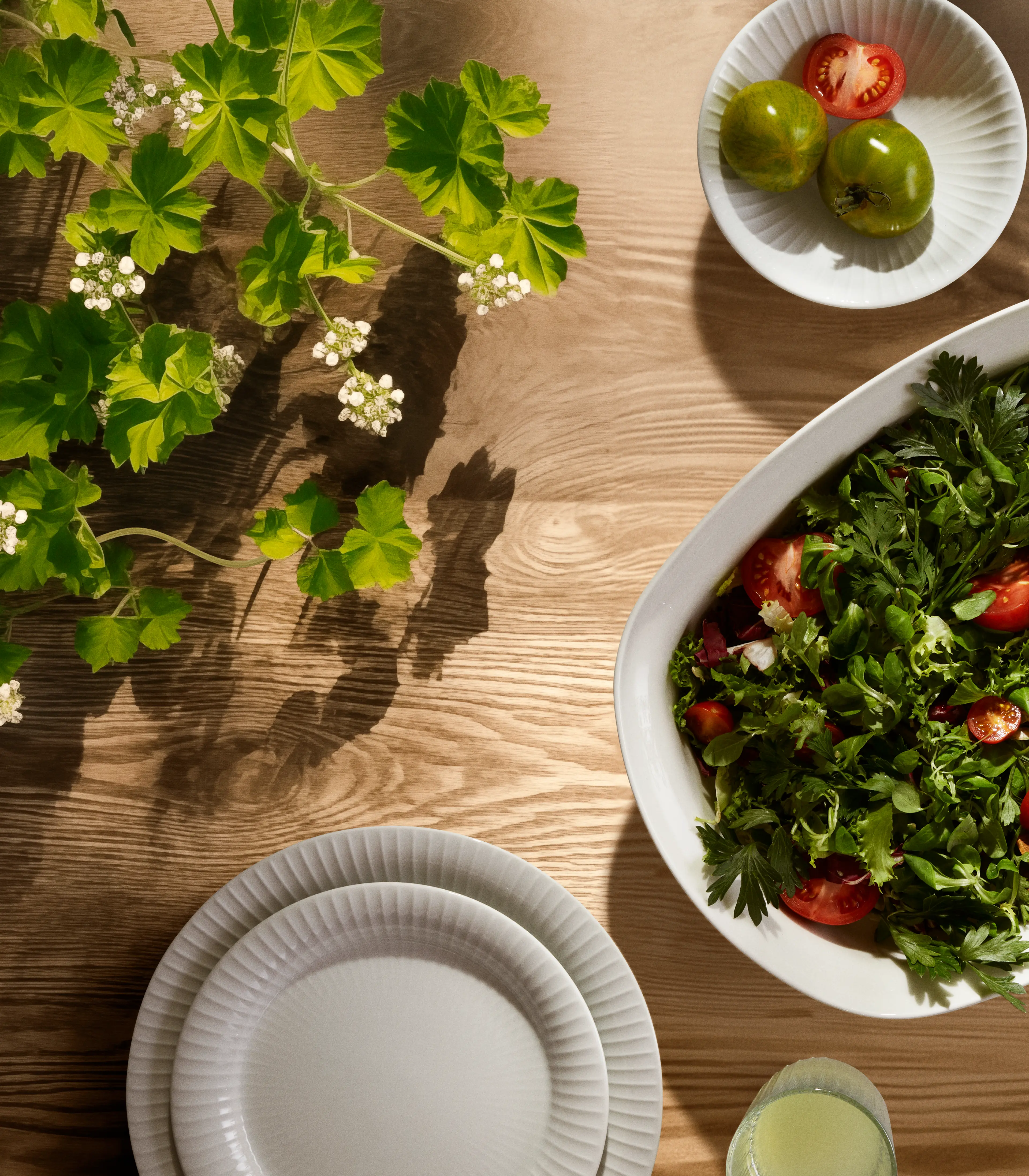 Kähler Hammershøi Geschirr mit Salat und Grün auf einem hellen Holztisch in natürlichem Ambiente.