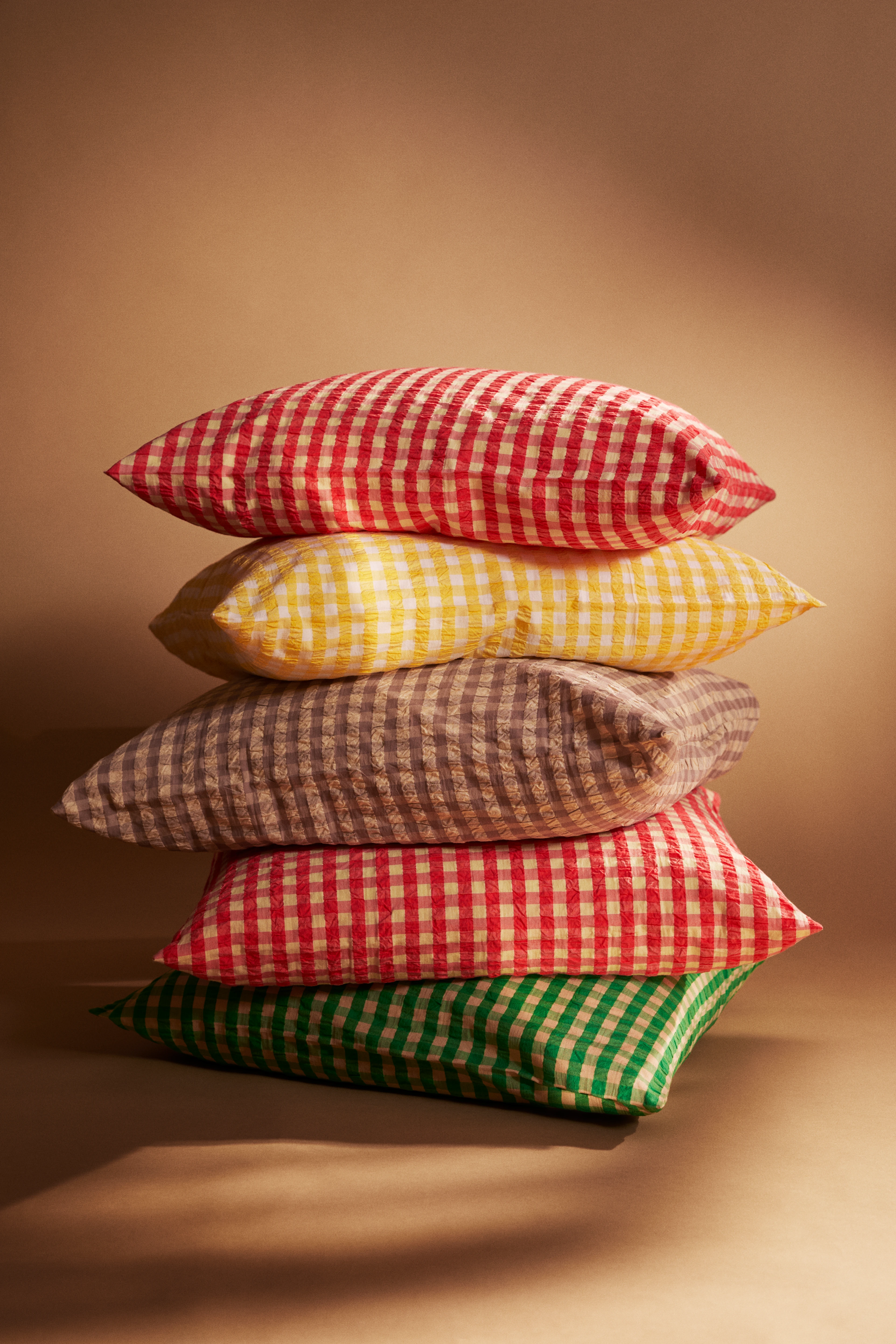 Five pillows from JUNA Bæk & Bølge stacked on top of each other in red, yellow, green, and sand
