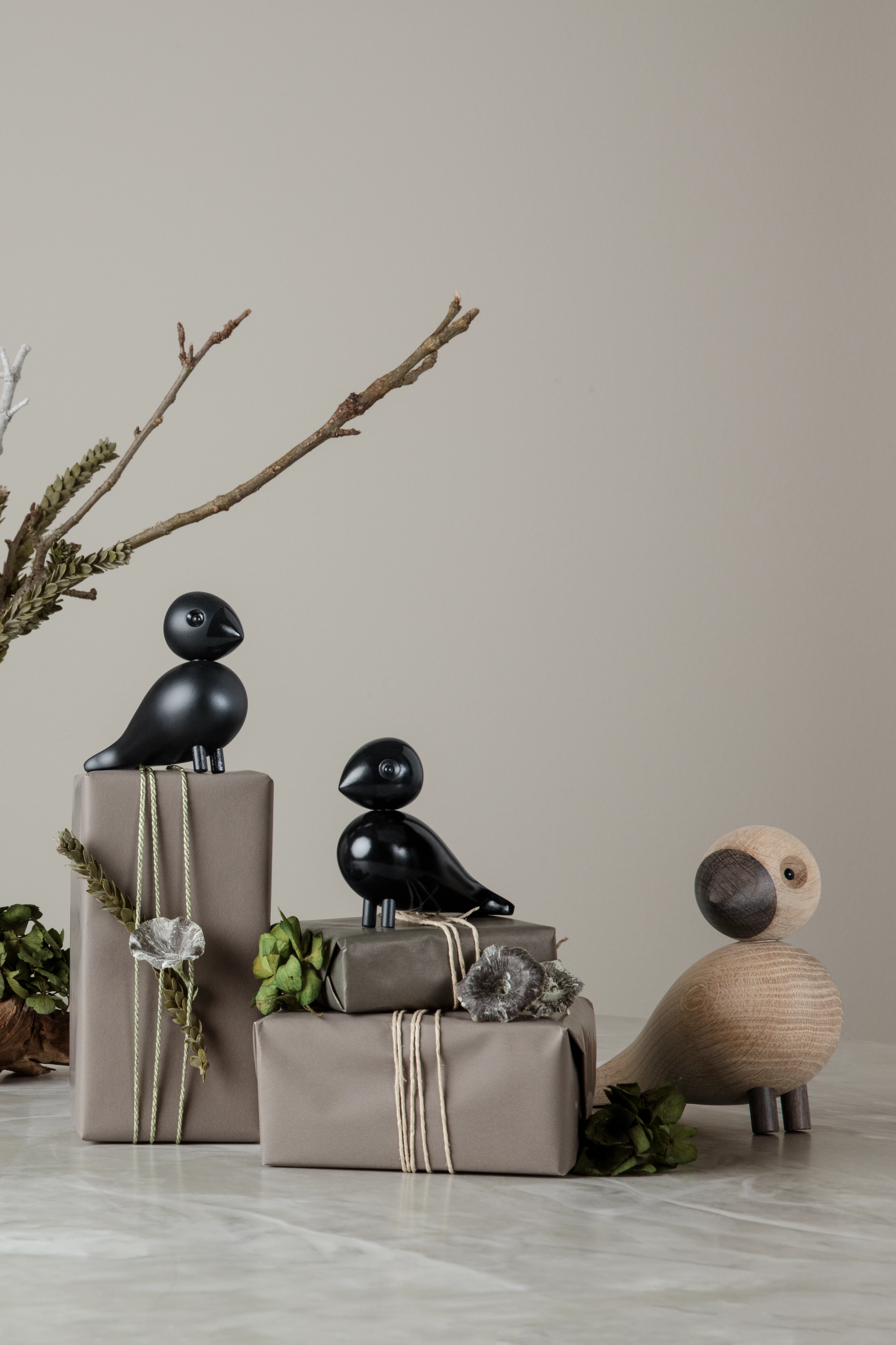 Kay Bojesen sangfugler plassert ved innpakkede gaver i dempede naturfarger, en rolig gaveoppsetning.