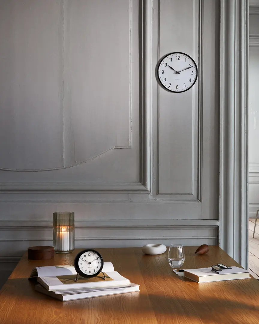 Arne Jacobsen Clocks Station wall clock and table clock styled on a desk in a calm, classic interior.