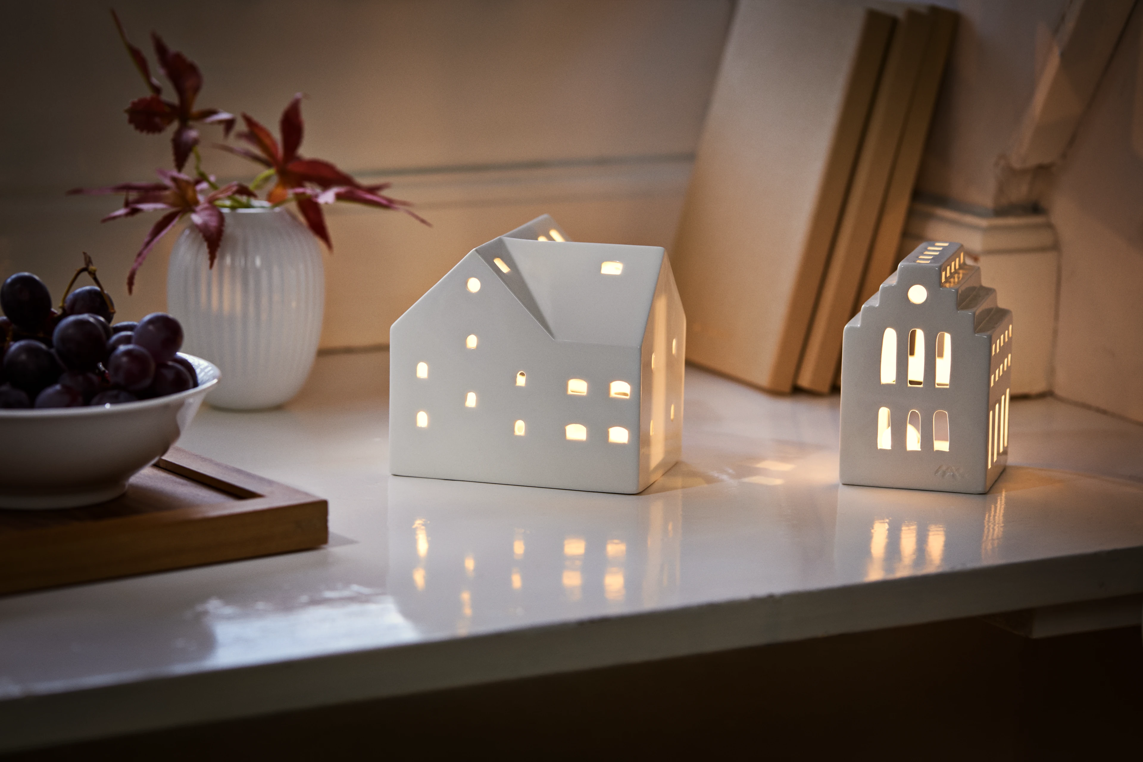 Two white ceramic house candle holders glowing on table, decorative set creating cozy warm ambiance