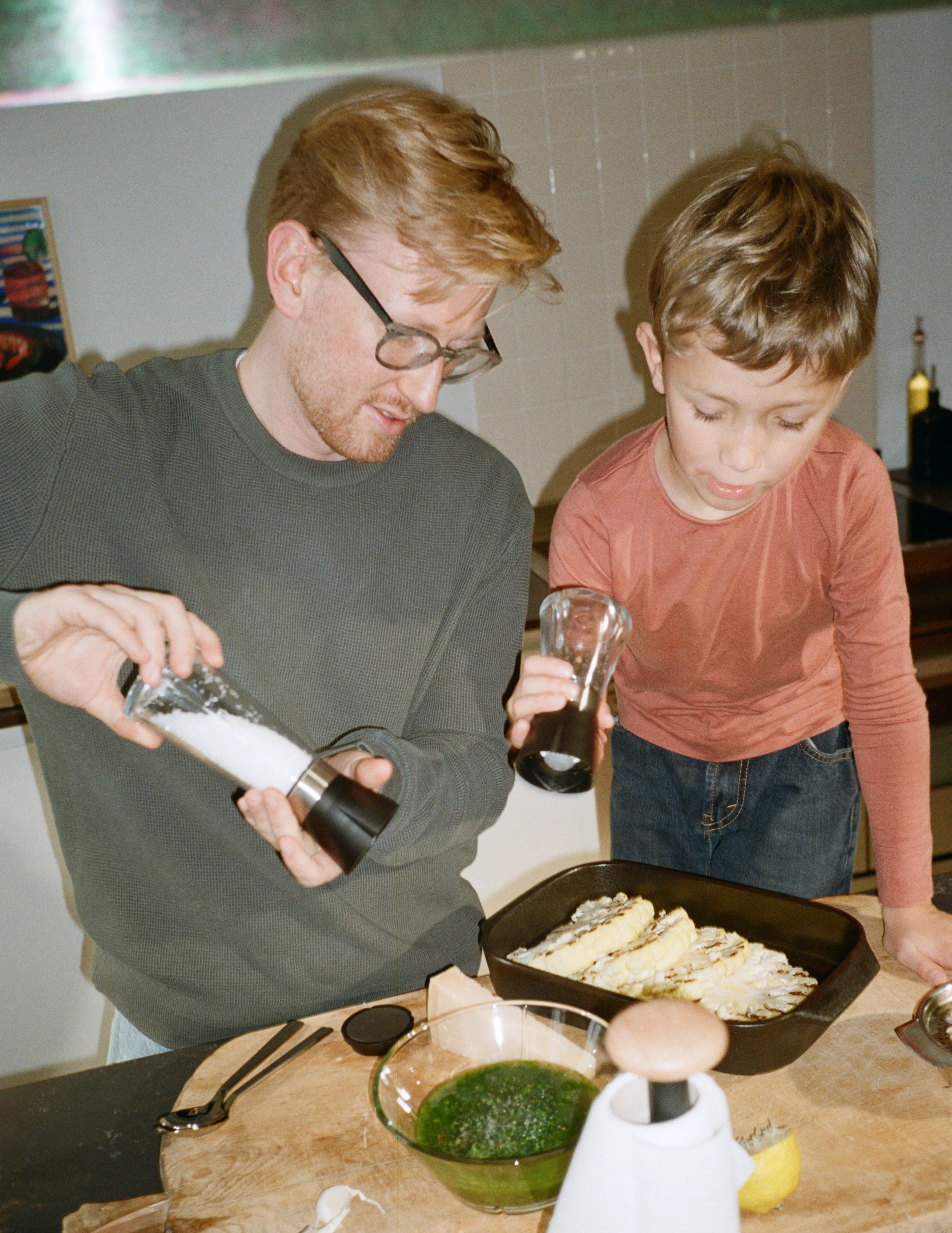 Two people cooking together at stove, seasoning dish in pan, cozy home cooking in kitchen