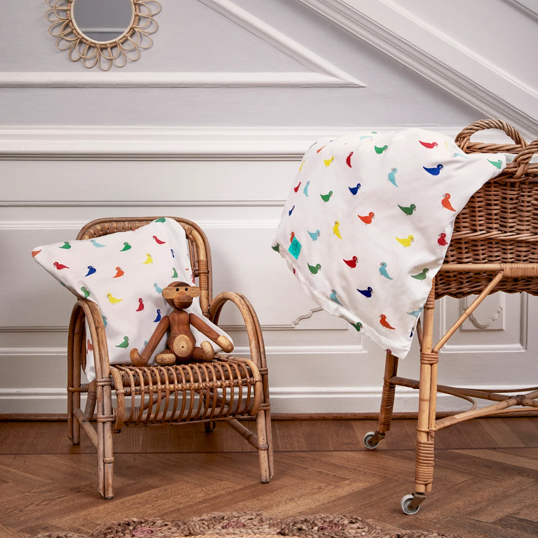 Rattan kids chair and doll stroller with colorful bird blanket and Kay Bojesen Babies in cozy setting