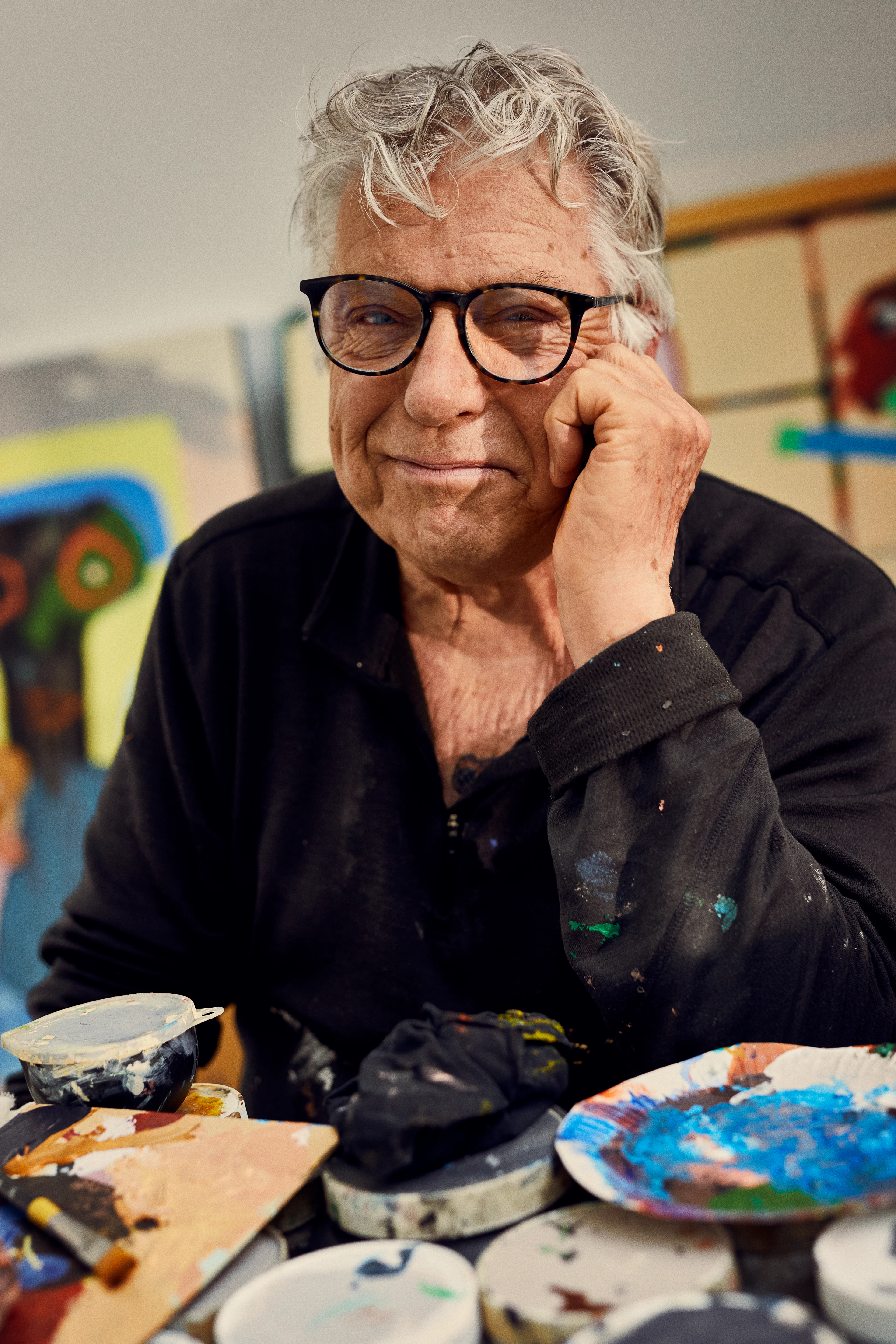 Leif Sylvester smiler med briller ved fargerikt kunstnerbord.