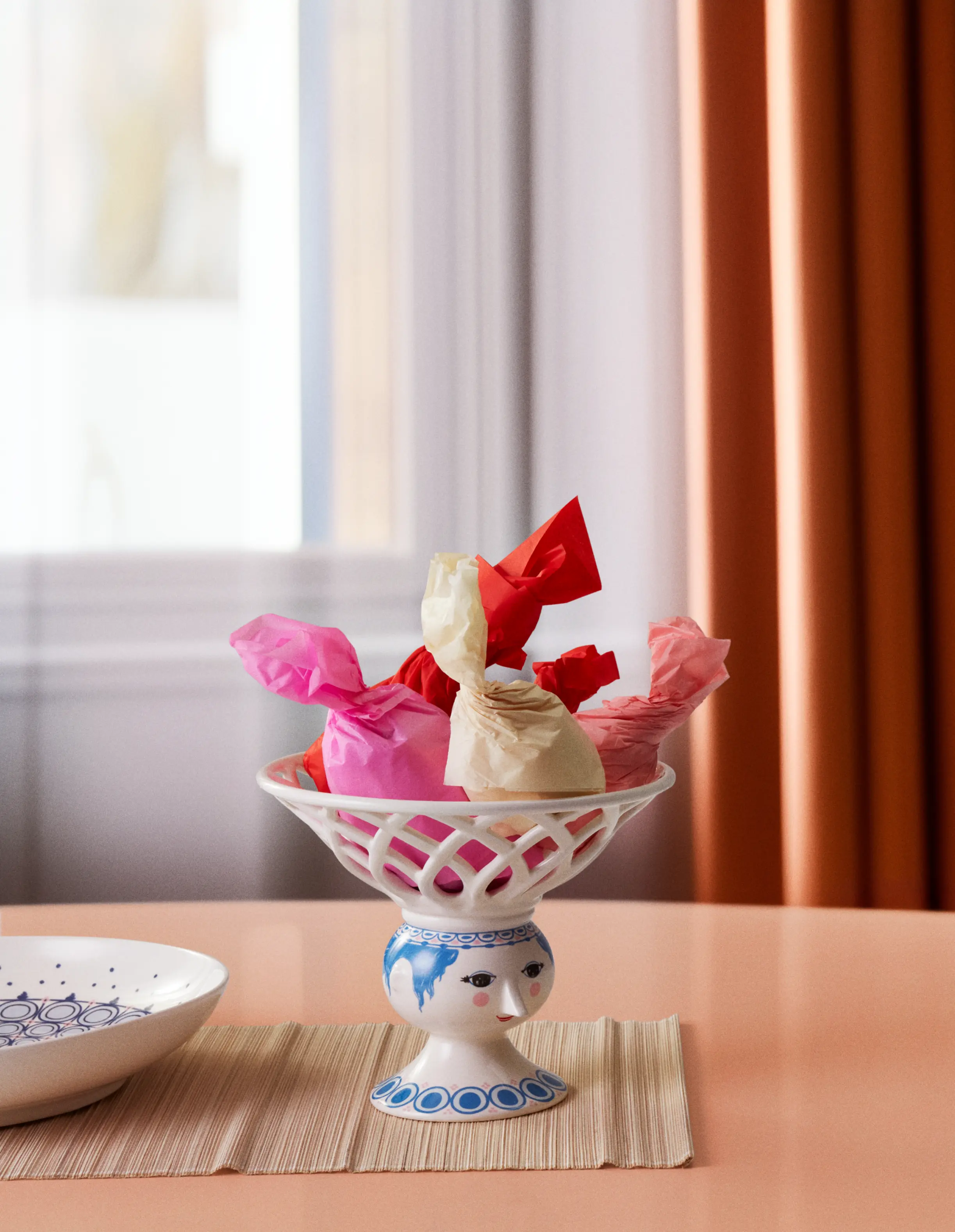 Bjørn Wiinblad Dora skål med färgglada inslagna praliner placerad på ett bord i ljus miljö.