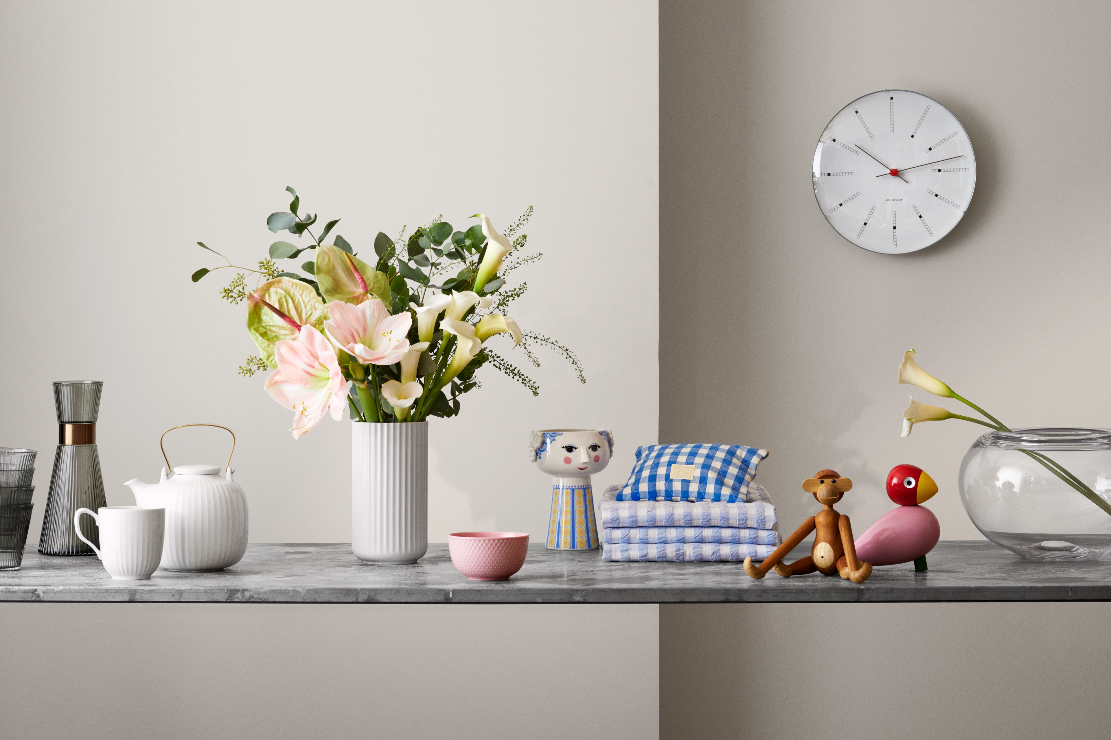 Stilleben med blomster, Kay Bojesen figurer, tekstiler og ur i lyse neutrale toner