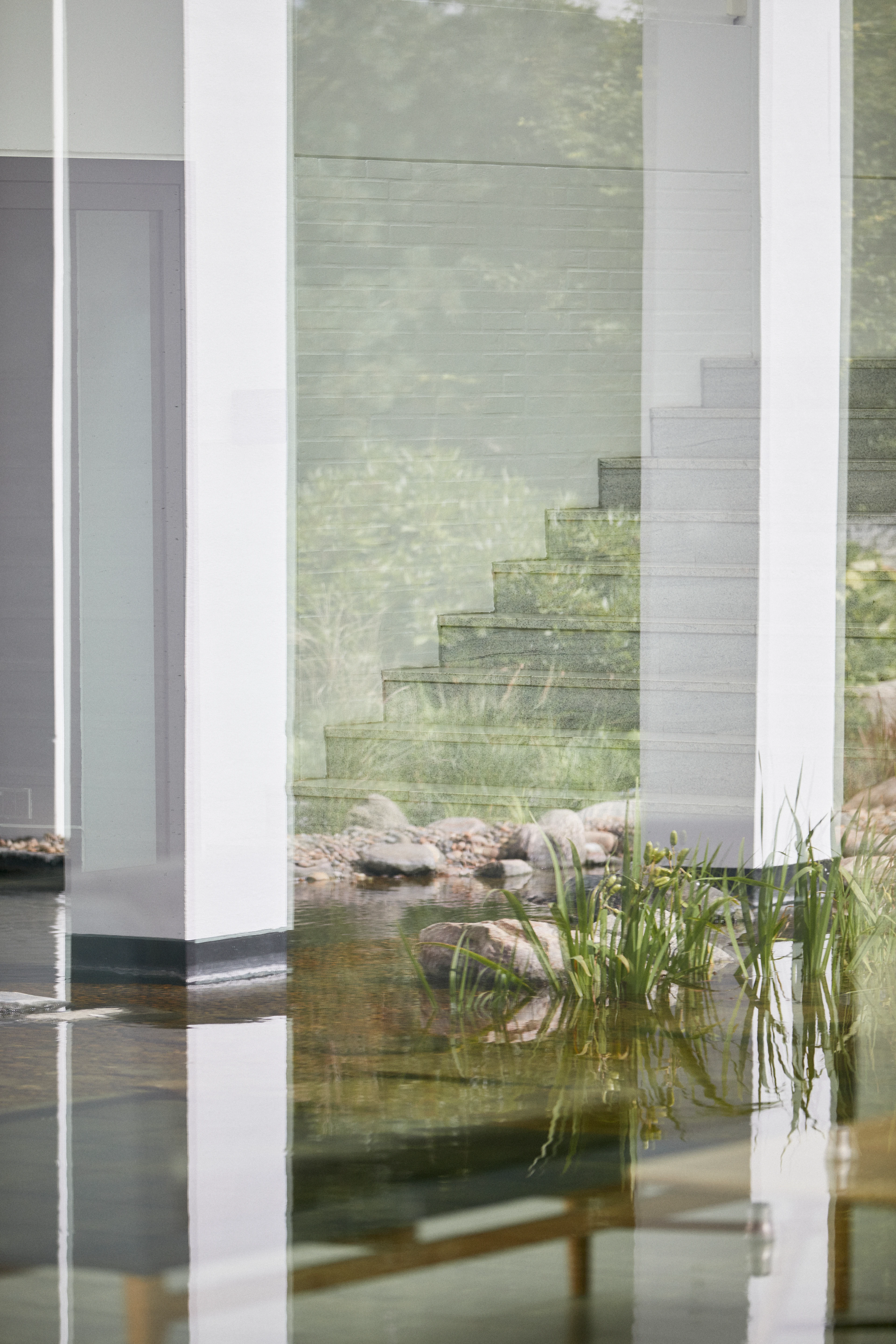 View from outside towards a building, featuring stairs leading inside, with reflections and water from a lake visible